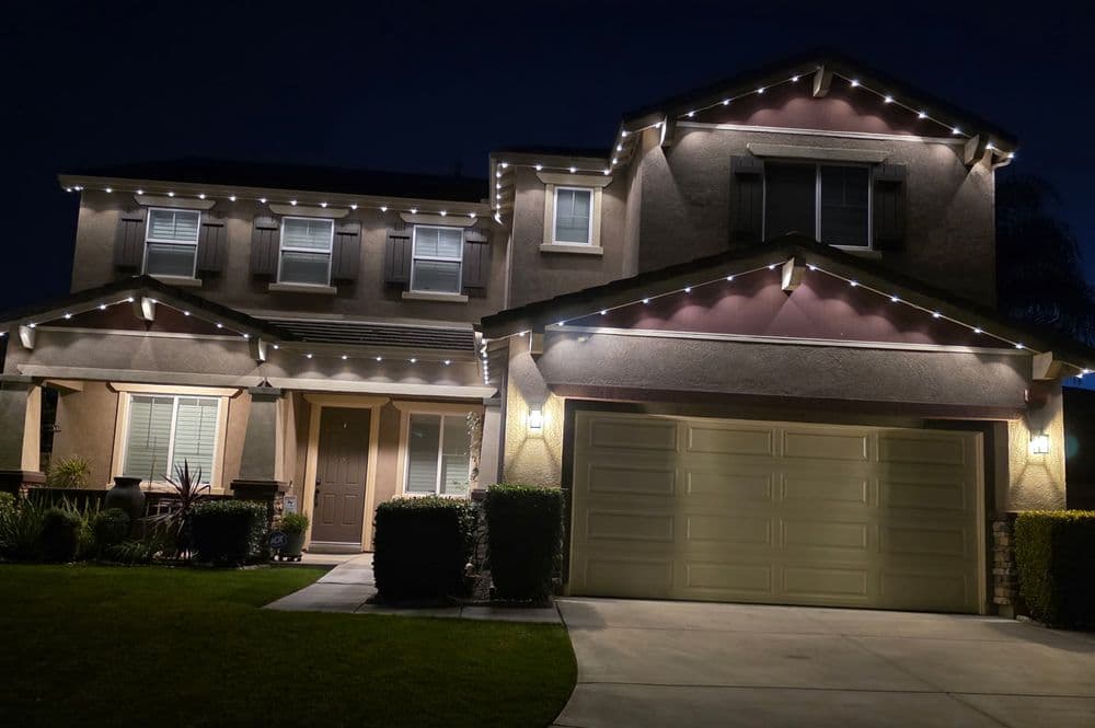 Modern suburban house with festive lights, well-maintained lawn, and a double garage at night.