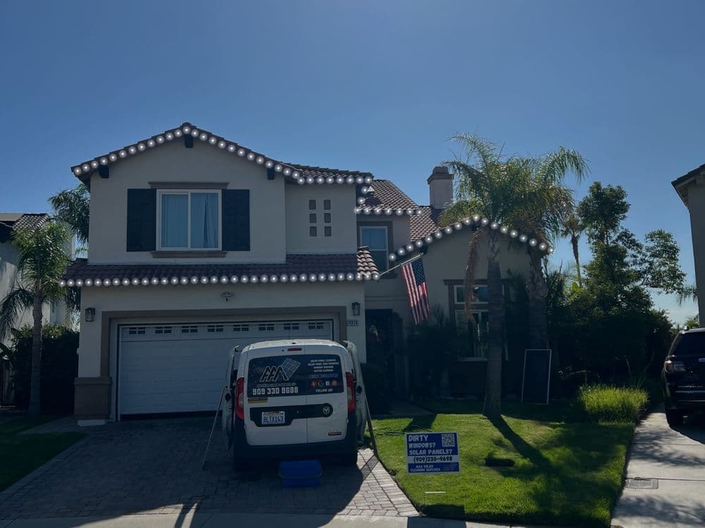 Two-story home decorated with lights, featuring a lush lawn and a parked service van.