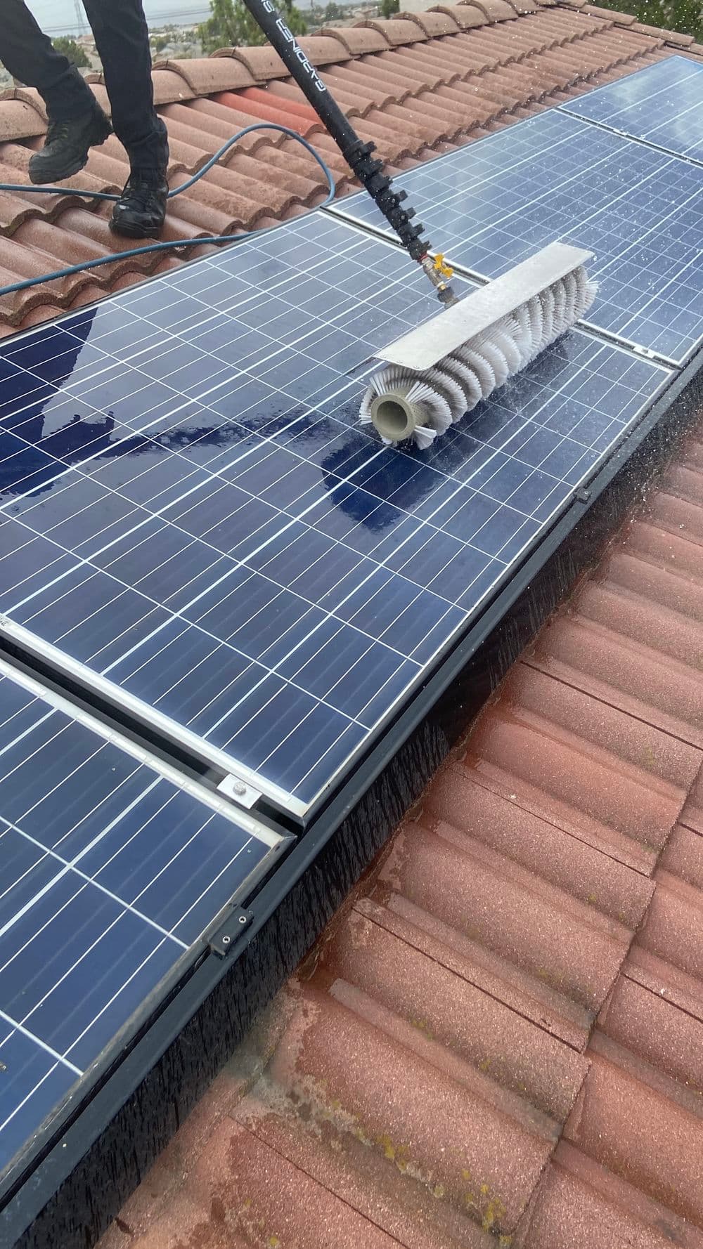 Cleaning solar panels on a rooftop with a specialized brush and water.
