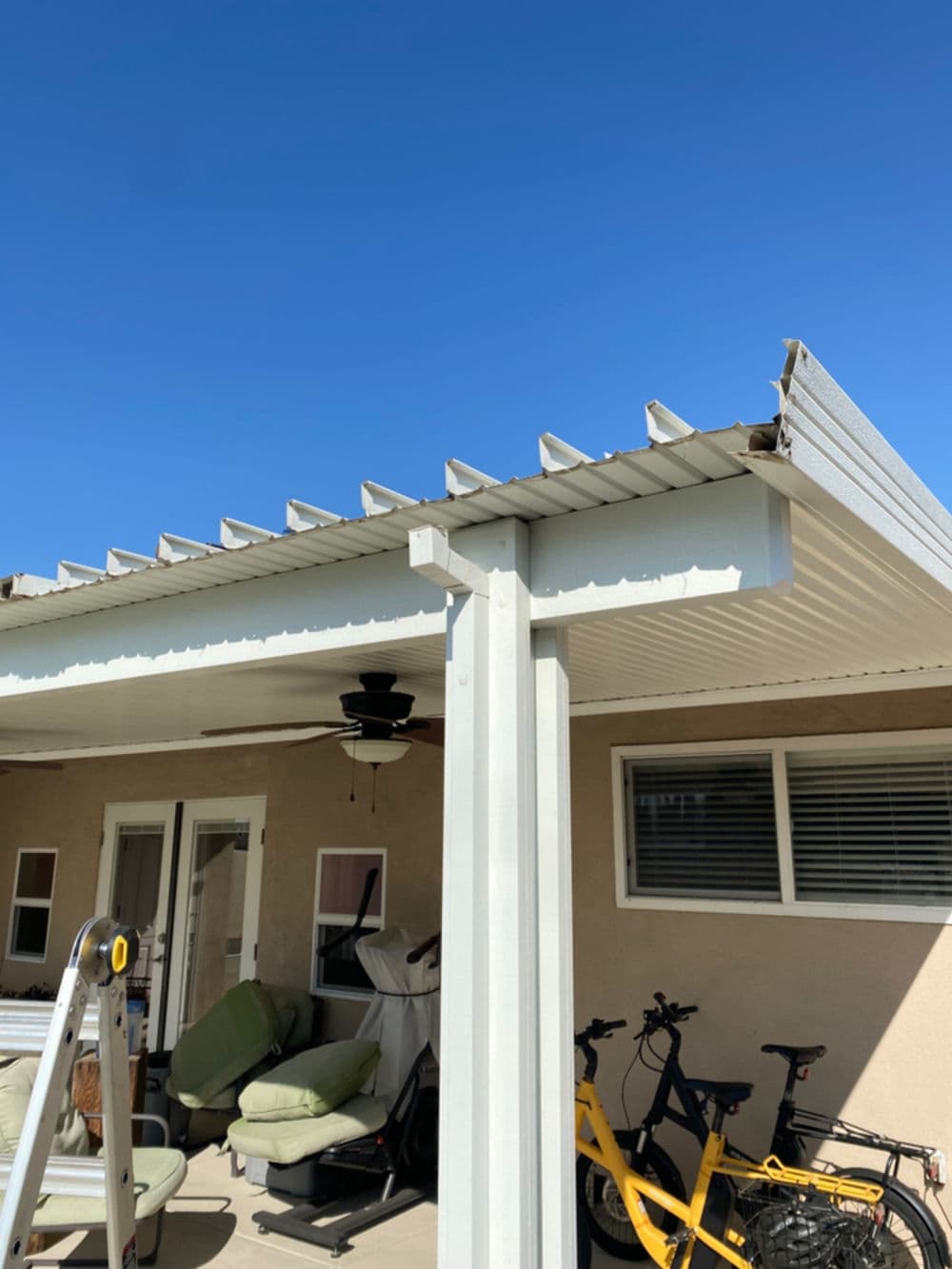 Covered patio with metal pergola, ceiling fan, and bicycles parked nearby against a blue sky.
