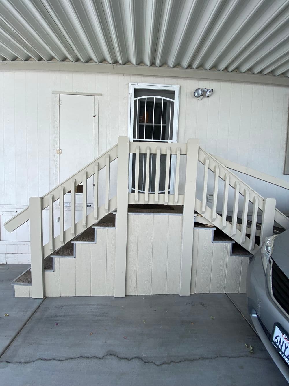 Sturdy beige stair ramp with railings leading to a door under a covered entryway.