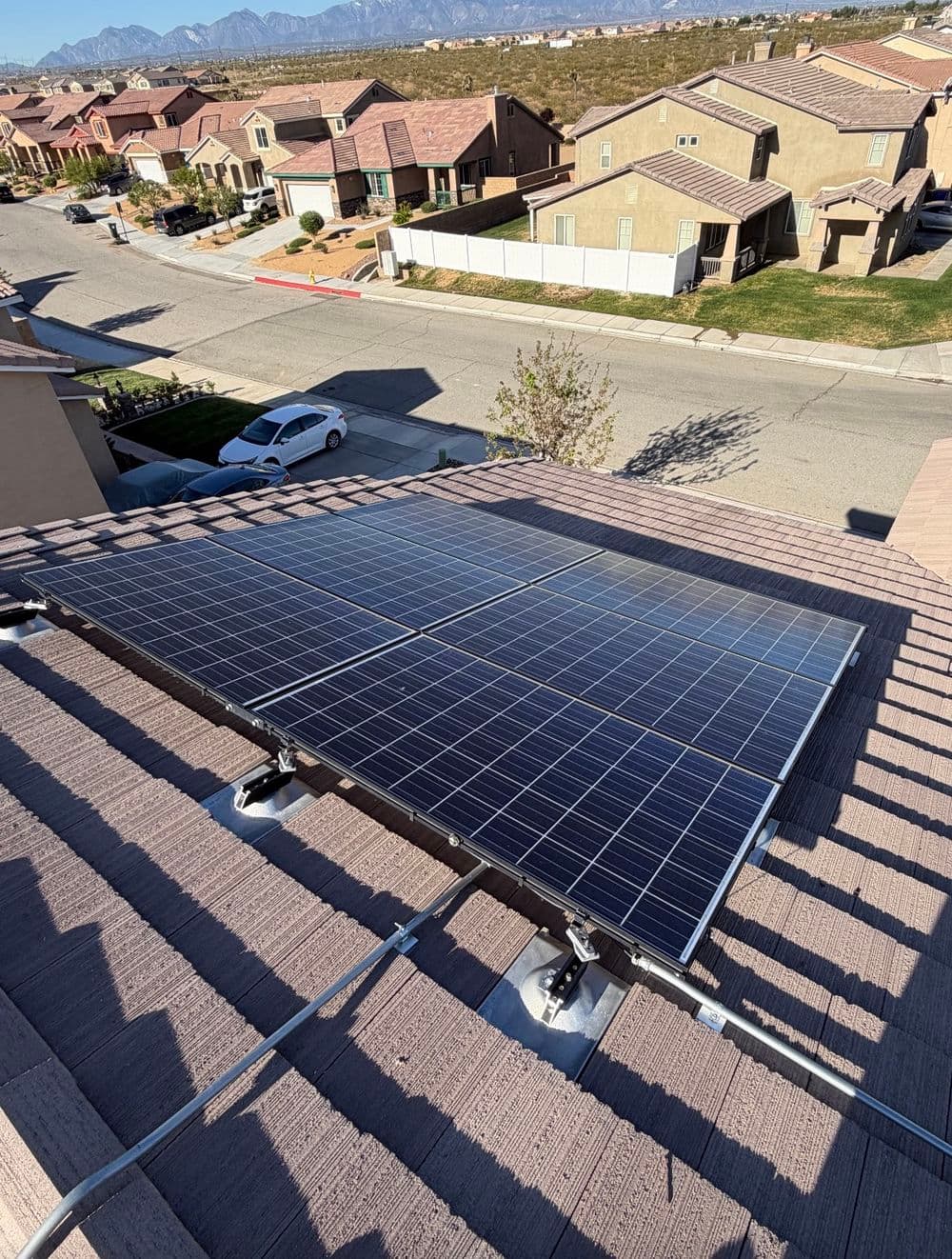 Solar panels installed on a rooftop in a suburban neighborhood with mountains in the background.