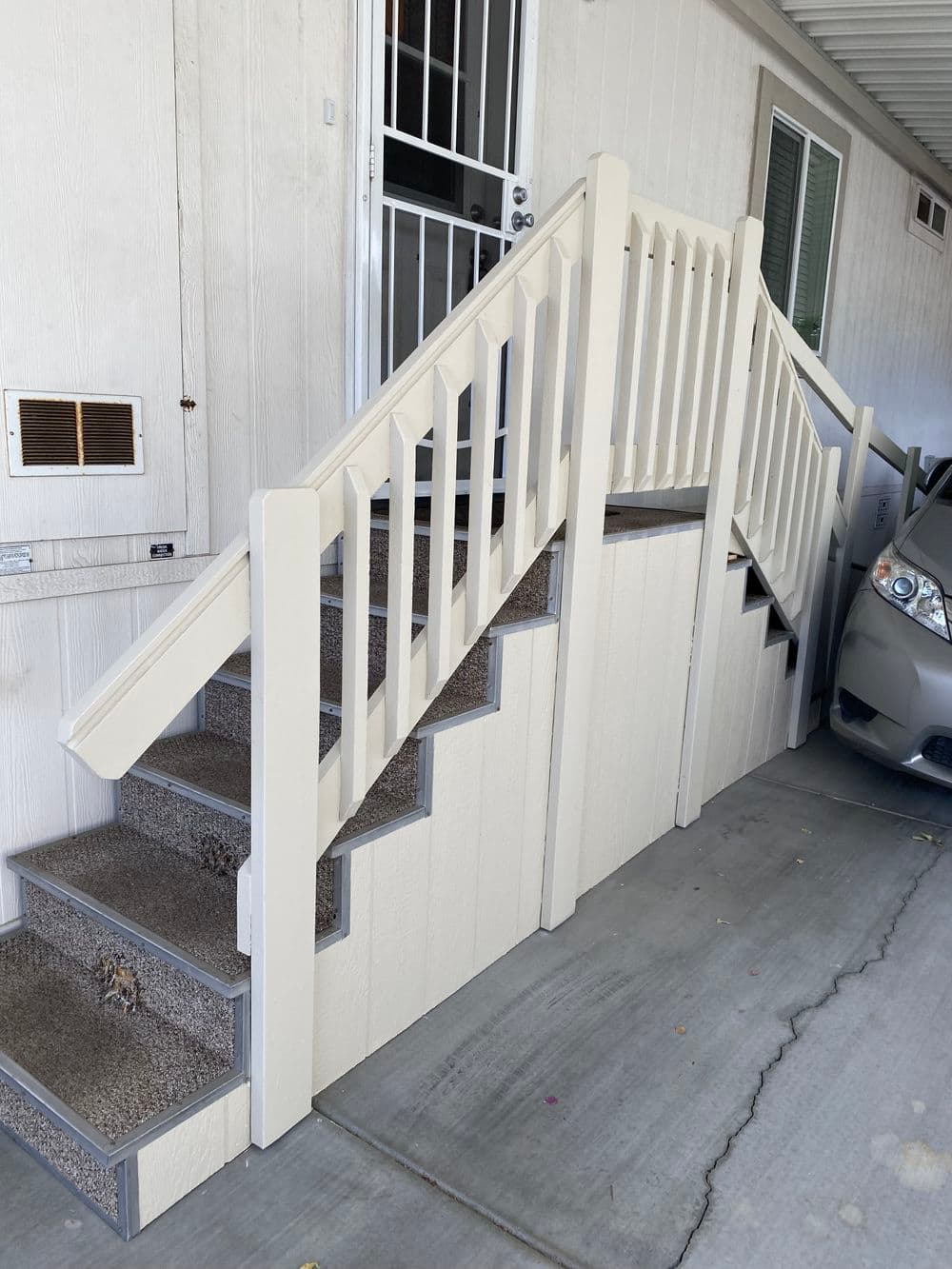 Sturdy outdoor stairs with white railing and carpeted steps leading to a doorway.