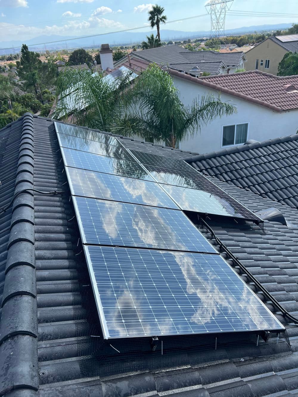 Solar panels installed on a roof with palm trees and blue sky in the background.