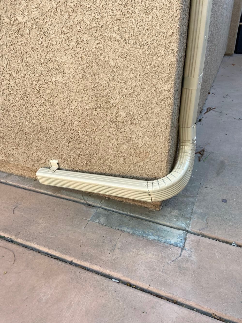 Corner rain gutter on textured wall with concrete ground, directing water runoff.