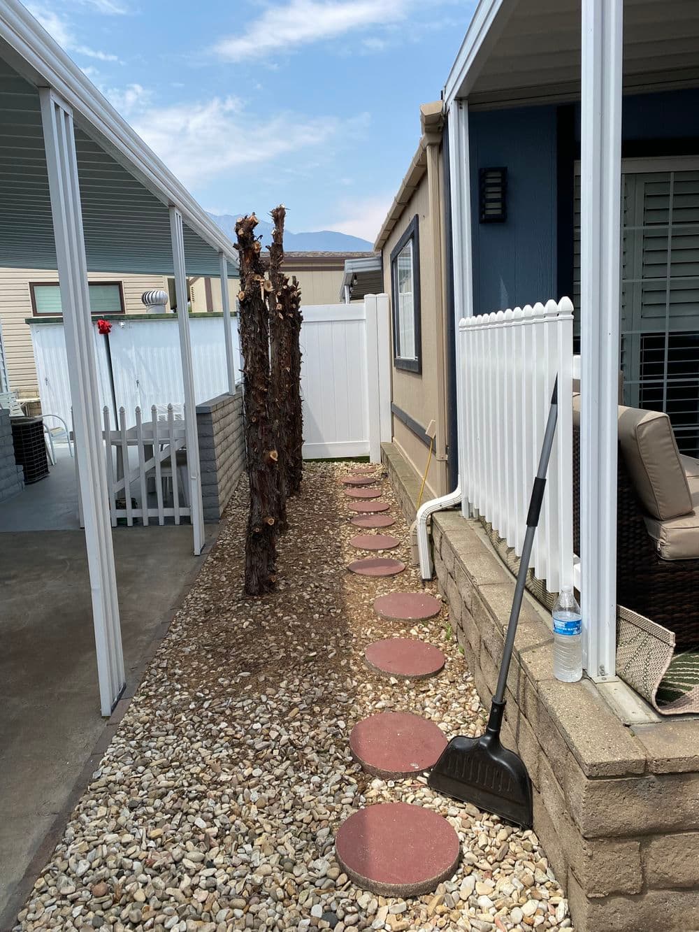 Garden pathway with stepping stones alongside a home, featuring a white fence and landscaping tools.