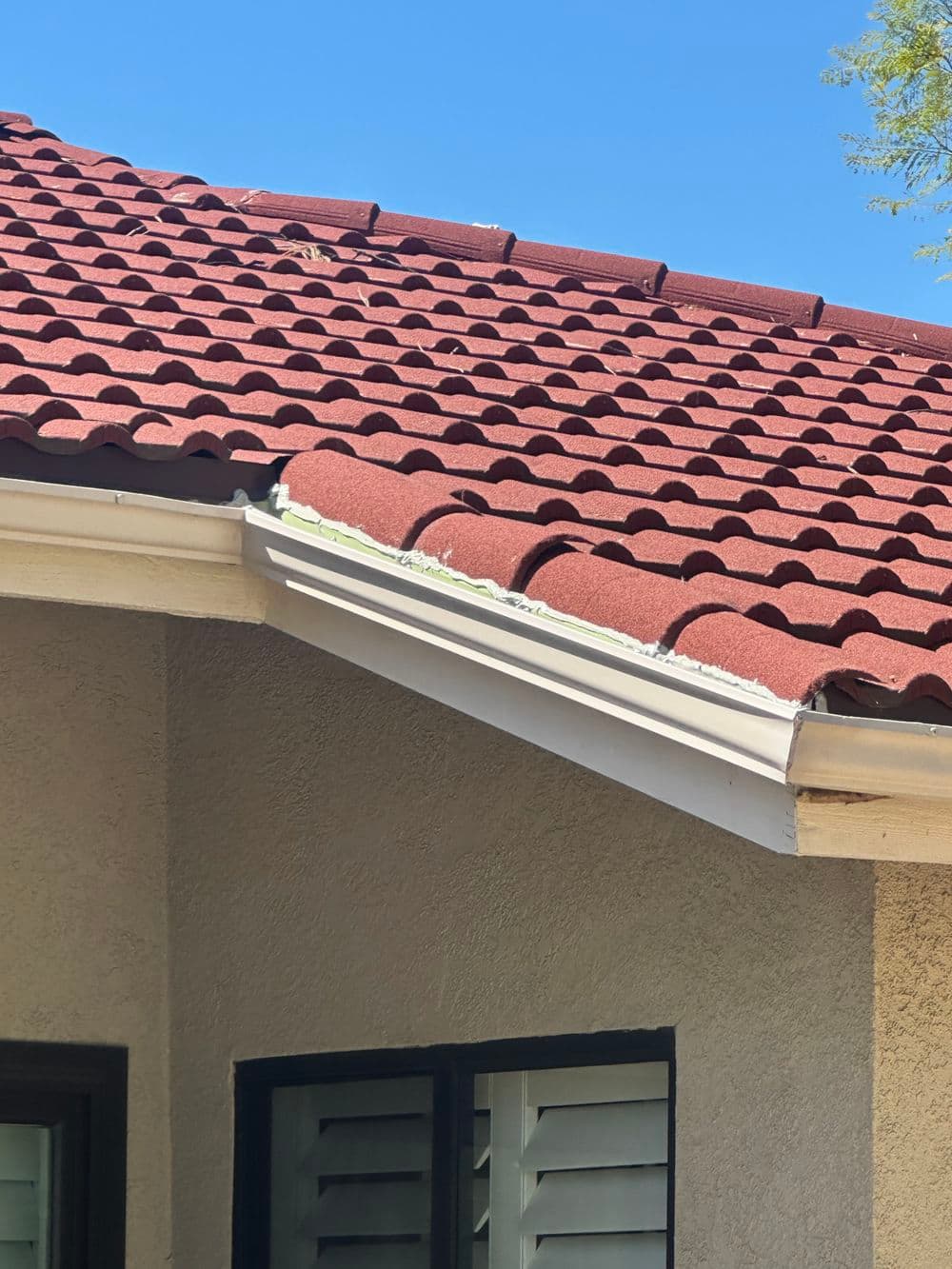 Red tiled roof with white guttering against a clear blue sky. Residential architecture detail.