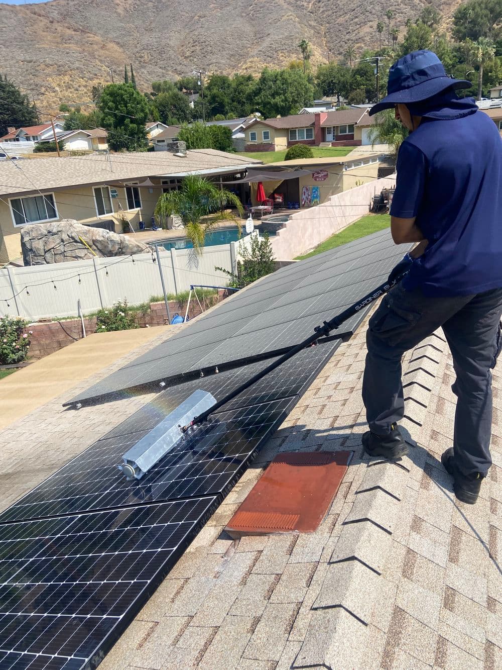 Person installing solar panels on a rooftop in a residential neighborhood, clear sky above.
