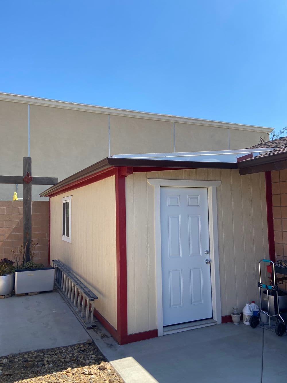 Exterior view of a small shed with a white door, red trim, and clear blue sky backdrop.