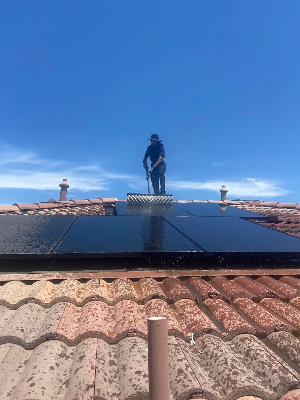 Worker cleaning solar panels on a rooftop under a clear blue sky.