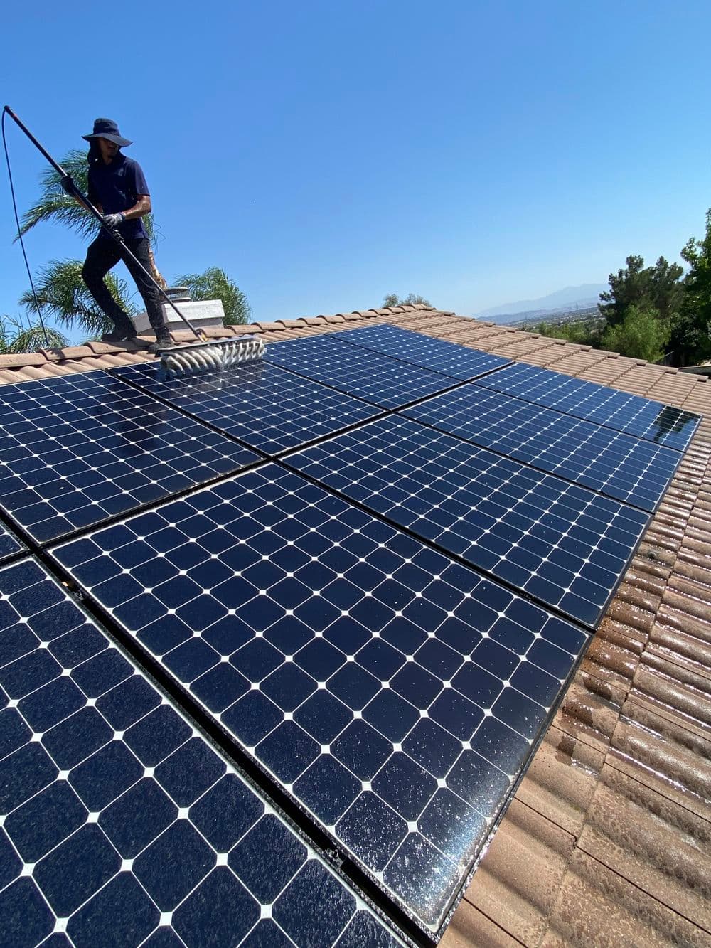 Worker cleaning solar panels on a rooftop under clear blue skies, promoting solar energy efficiency.