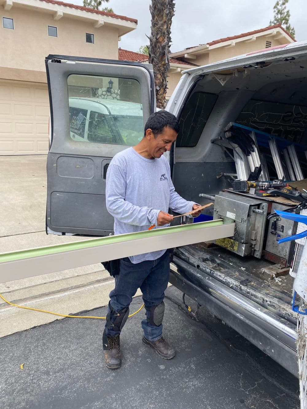 Worker measuring material at van for home improvement project in sunny neighborhood.