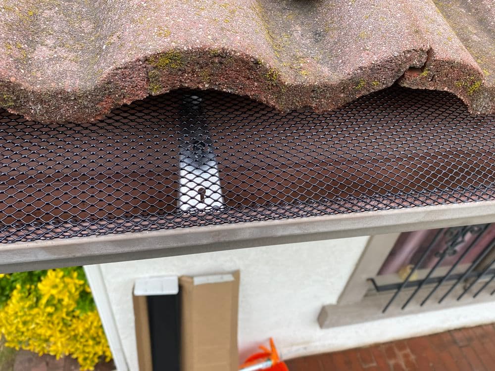 Close-up of a roof gutter with black mesh protection and moss-covered tiles.