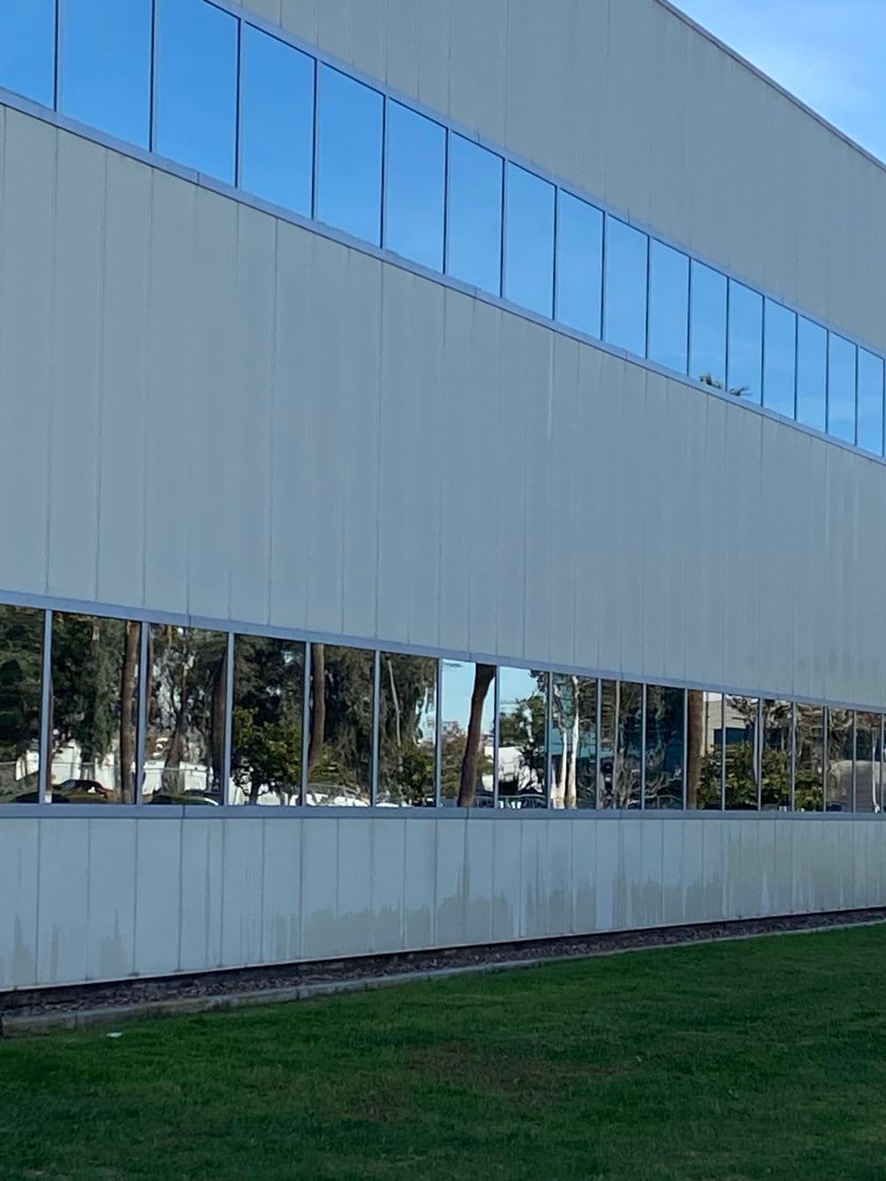 Modern building exterior with reflective windows and green grass landscaping.