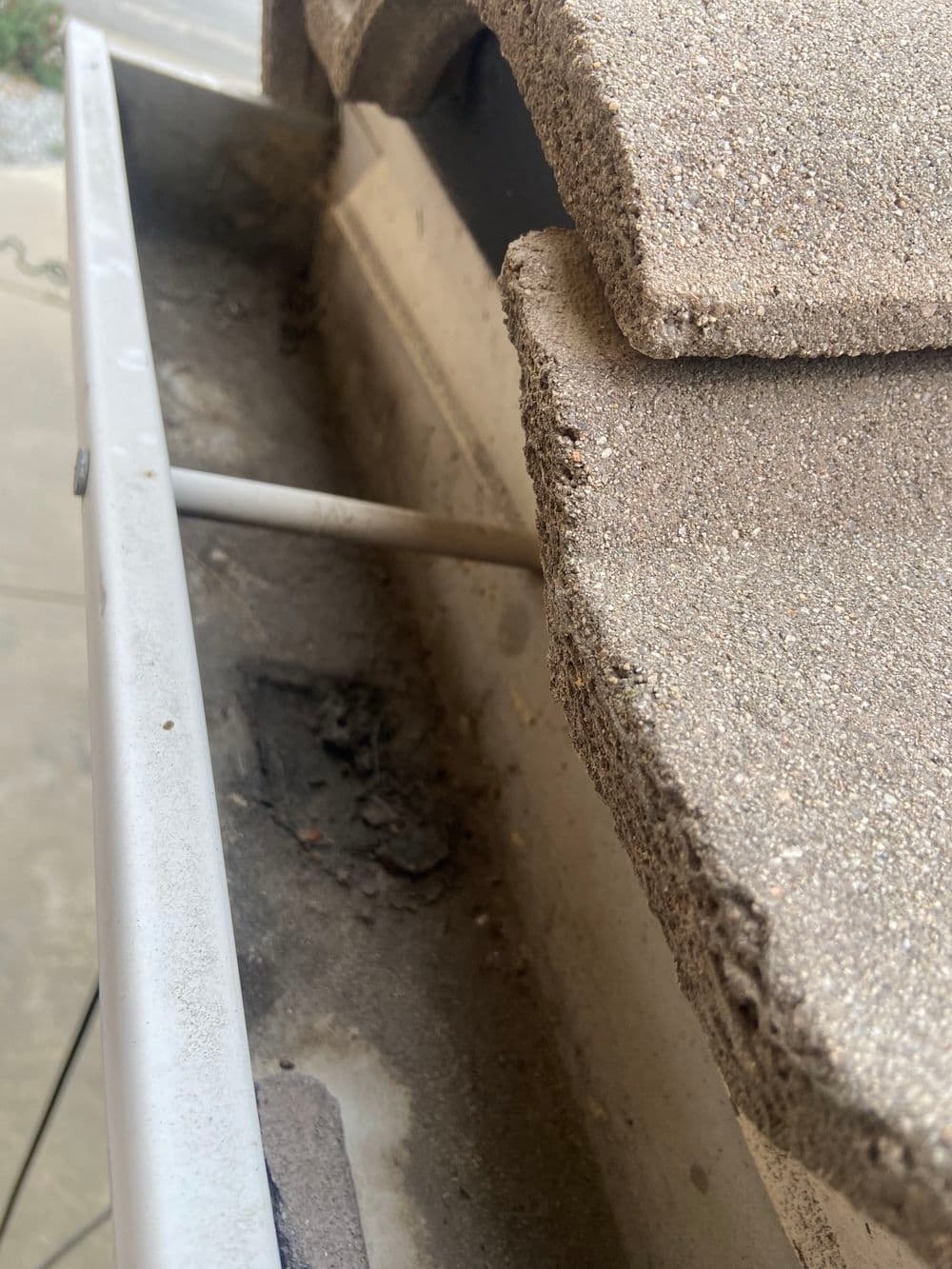 Clogged gutter with debris and roof tiles blocking drainage system.
