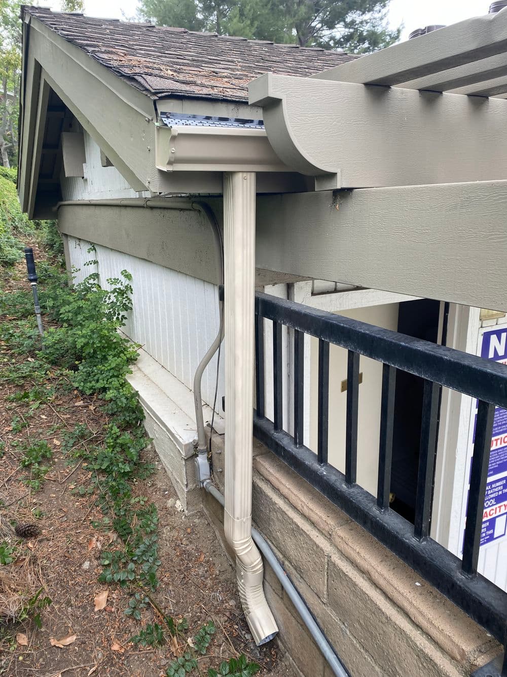 Gray downspout attached to house exterior, directing rainwater away from foundation.