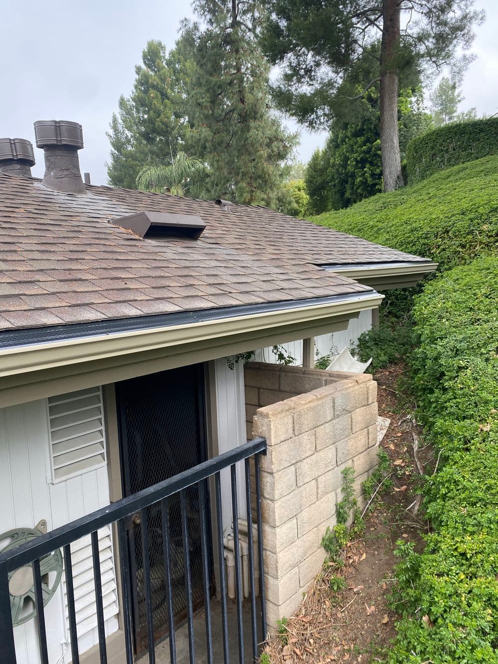 Residential building with a sloped roof and greenery surrounding a fenced entrance.