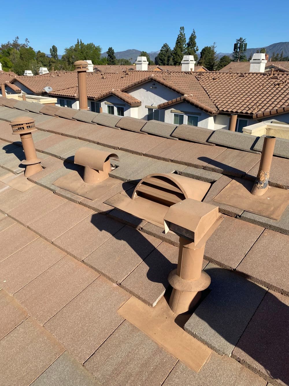 Roof vent pipes and architectural details on a residential roof in clear blue sky.