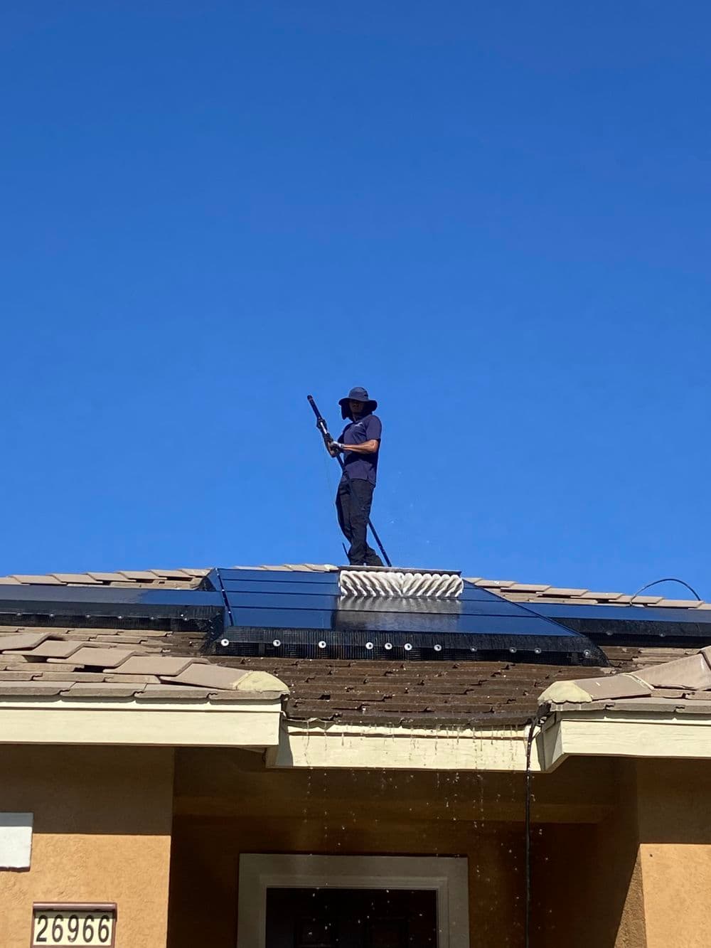Worker cleaning rooftop solar panels under a clear blue sky.
