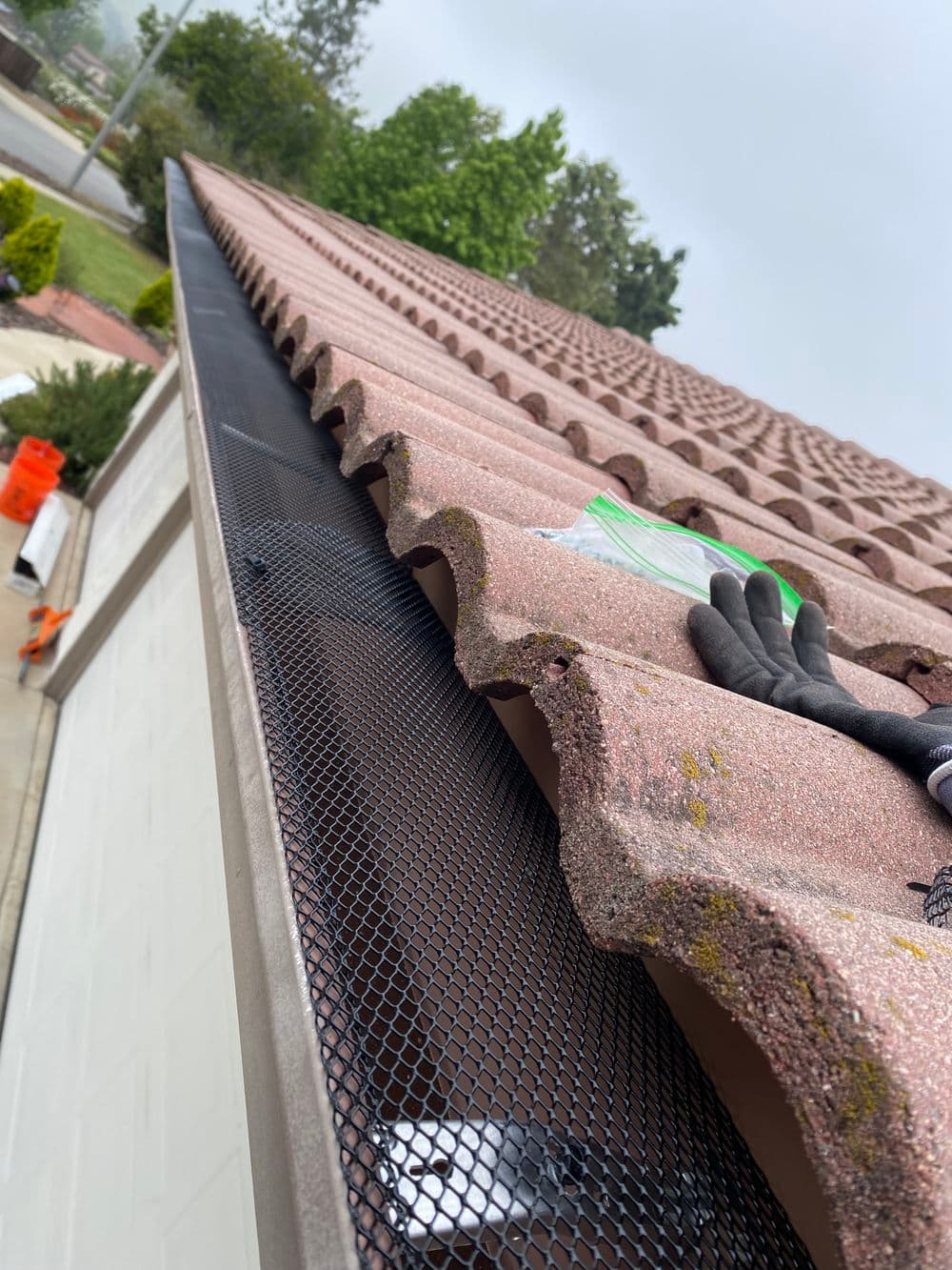 Installation of mesh gutter guard on a clay tile roof for debris protection.