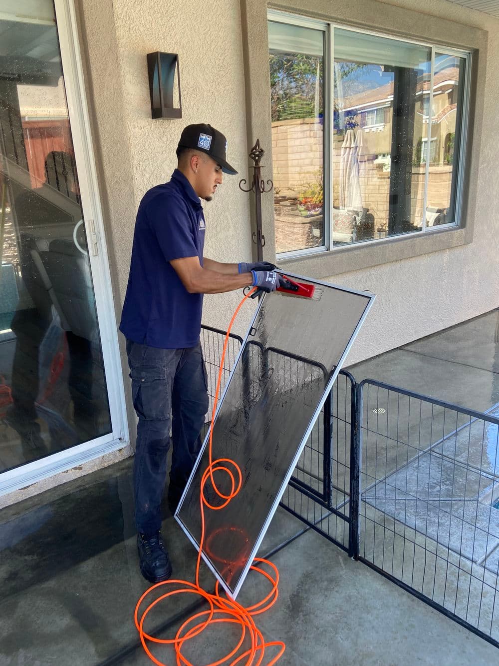 Worker cleaning a large glass panel outdoors with an electric tool and safety gloves.
