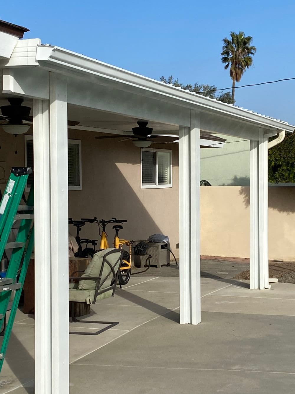 Modern patio cover with white columns, ceiling fans, and bicycles in the background.