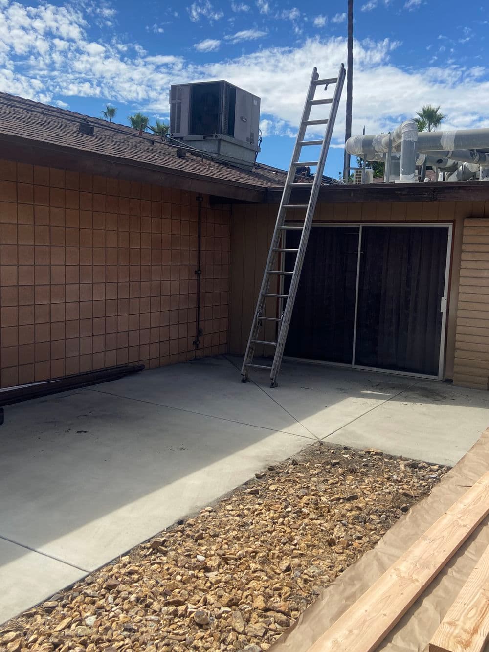 Metal ladder leaning against a house rooftop with an HVAC unit in the background on a sunny day.