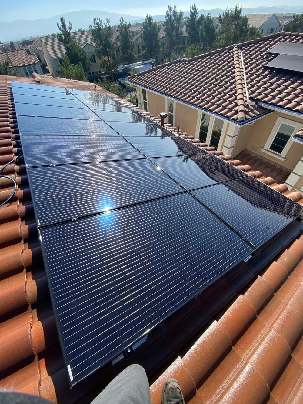Solar panels installed on a rooftop, reflecting sunlight, with homes in the background.