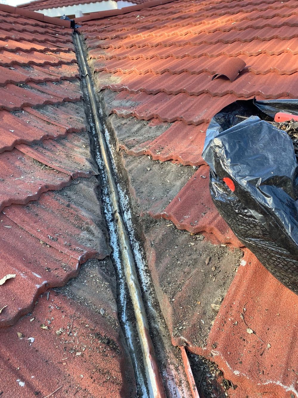 Clogged roof gutter with debris and dirt on a red tile roof.