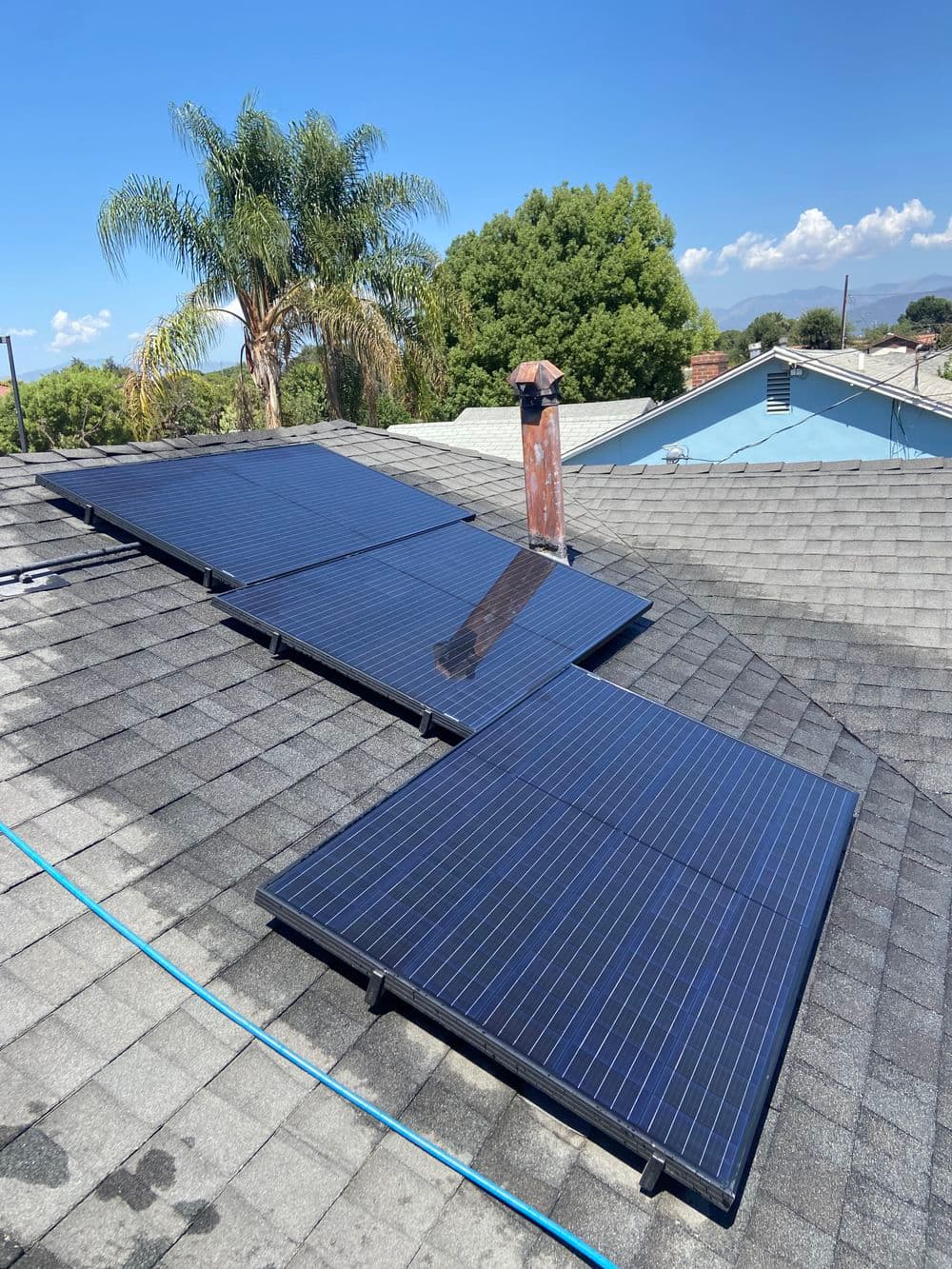 Solar panels installed on a sloped roof, surrounded by trees and a clear blue sky.