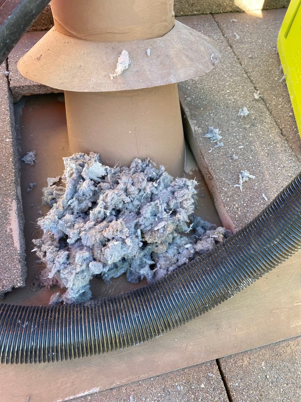 Dried lint accumulation around a ventilation pipe on a roof, with adjacent vacuum hose.