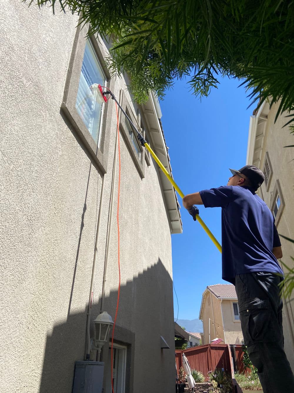 Man using a pole to clean a high window on a residential building outdoors.