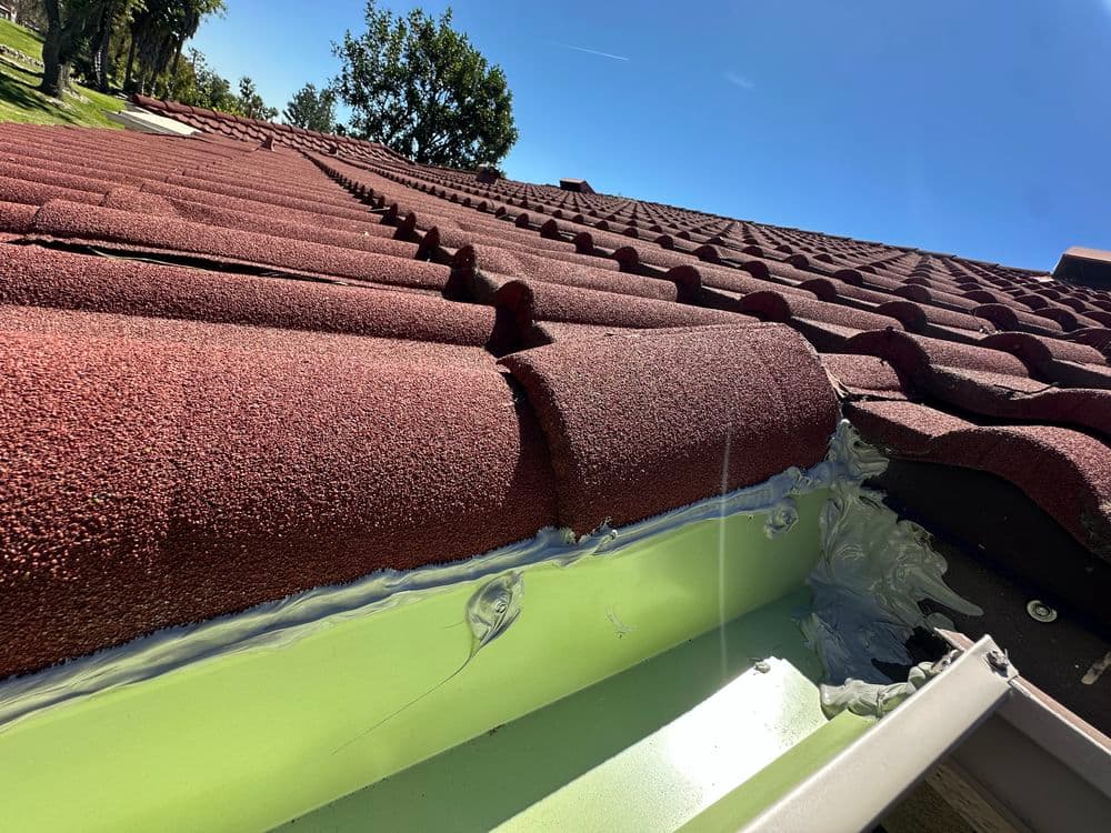 Roofing shingles with texture, showing detail of gutter installation and clear blue sky.