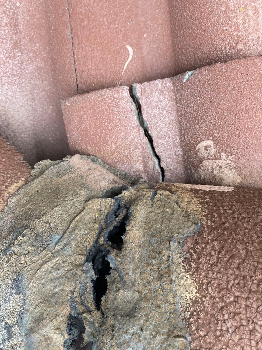 Cracked and damaged roofing tiles with visible deterioration and soil buildup.