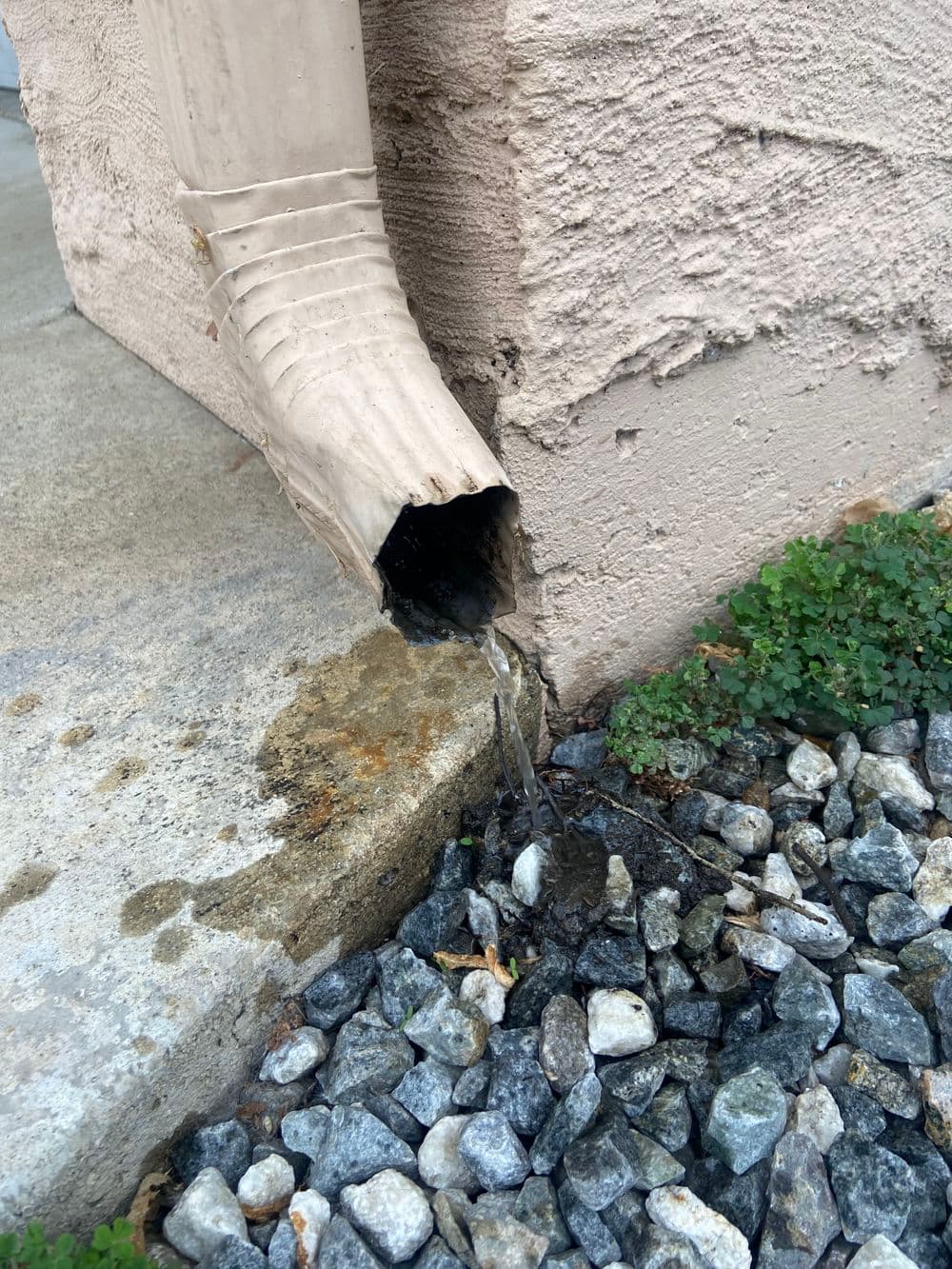 Downspout discharging water onto gravel surface near building foundation.