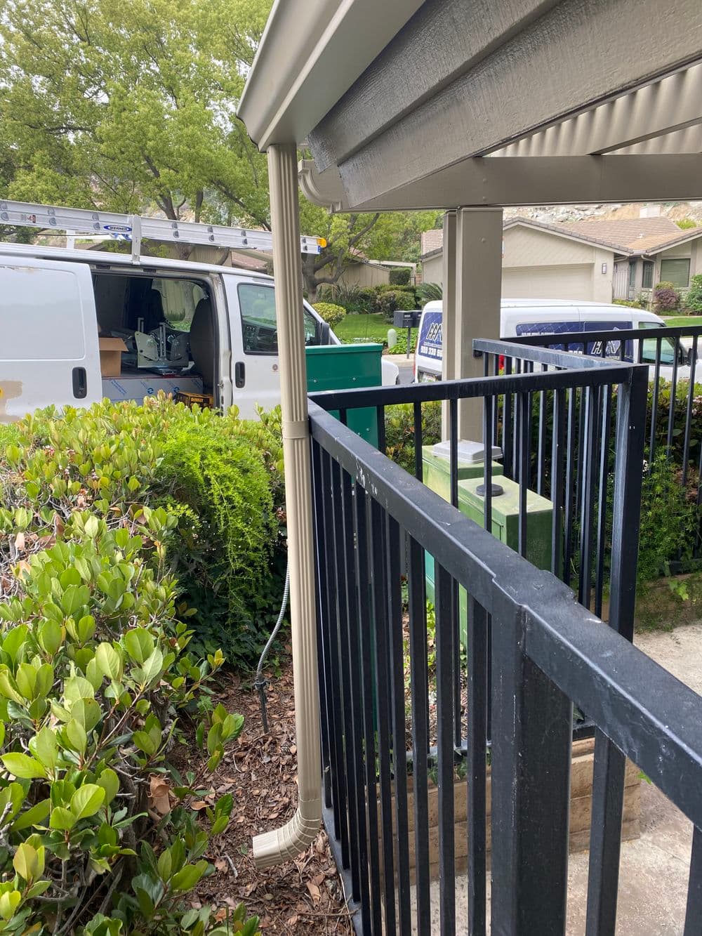 Downspout leading to a drainage system beside a black fence and service van in the background.