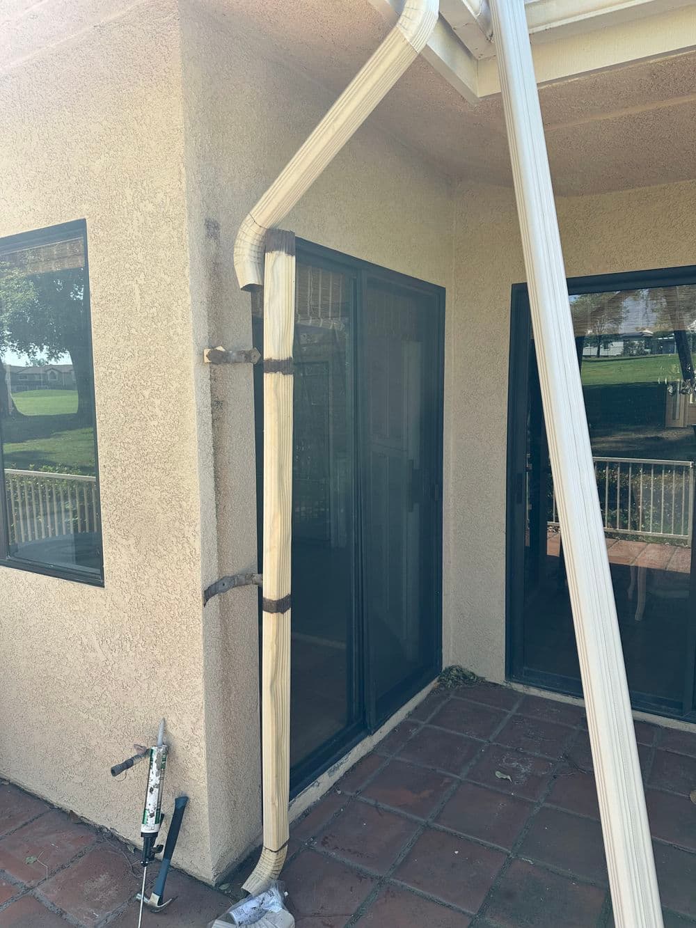 Exterior view of a house featuring a downspout, sliding doors, and patio tiles.